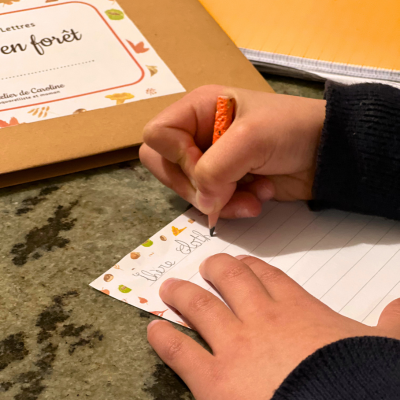 Un enfant écrit une lettre au crayon de bois.