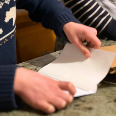 Un enfant glisse sa lettre pliée dans une enveloppe.